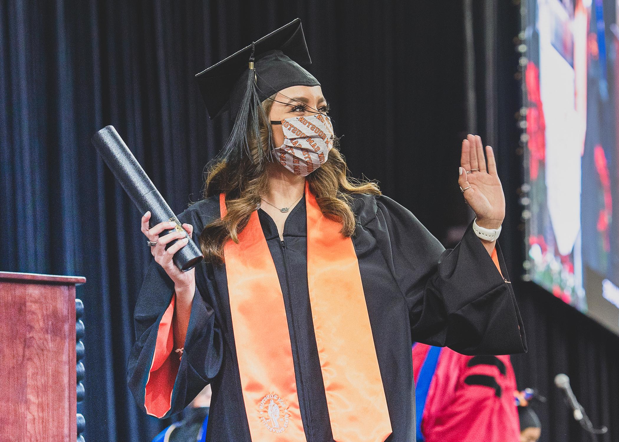 Student standing on Commencement stage holding a diploma and waving