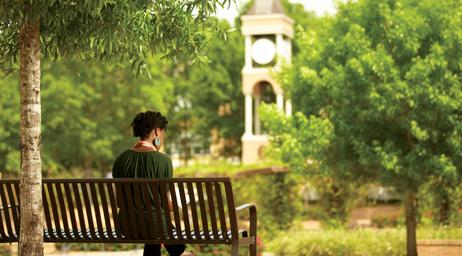 一个学生正坐在mgm集团线路检测中心钟楼前的长凳上思考.